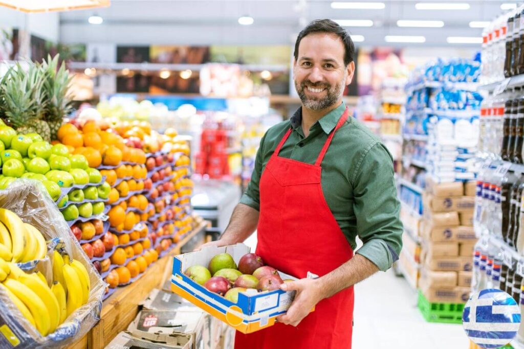 greece supermarket staff holding fruits in middle isle wearing a red aipron